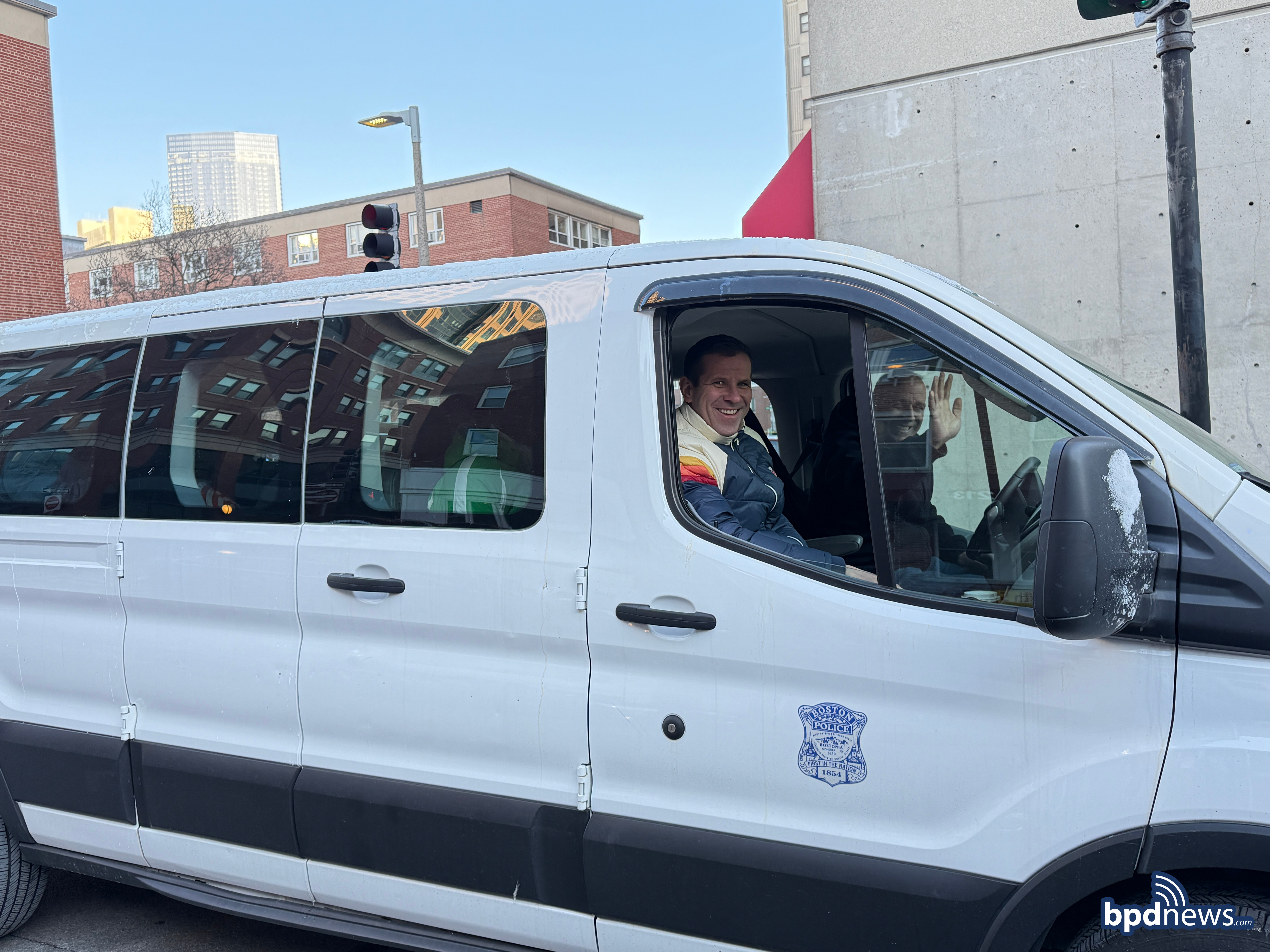 Officers from District A-1 in a van waving to camera as they prepare to drive community members to Wachusett Mountain to learn to snowboard