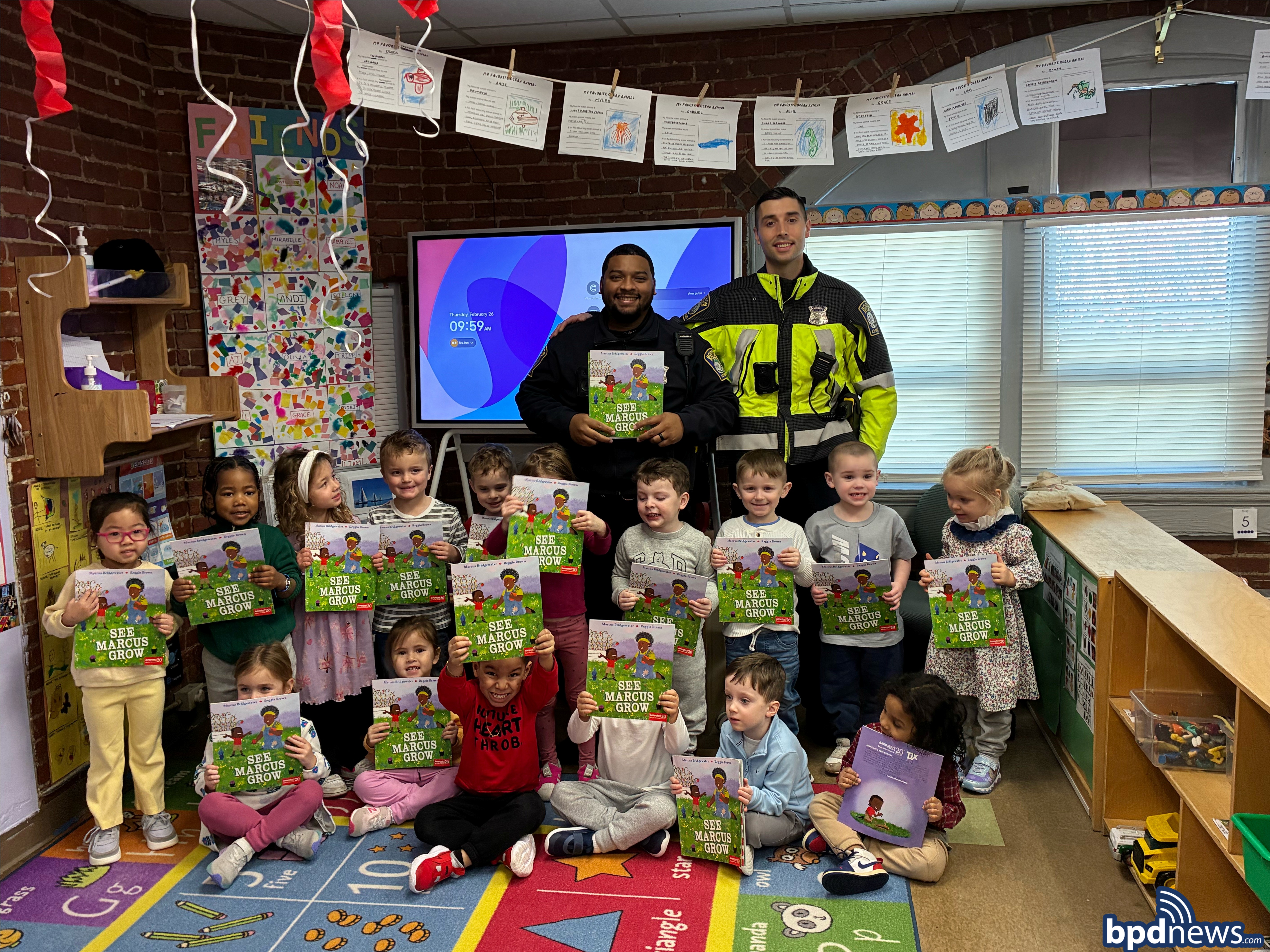 Boston Police Officers pose for picture with students as they all hold up the book that was read.