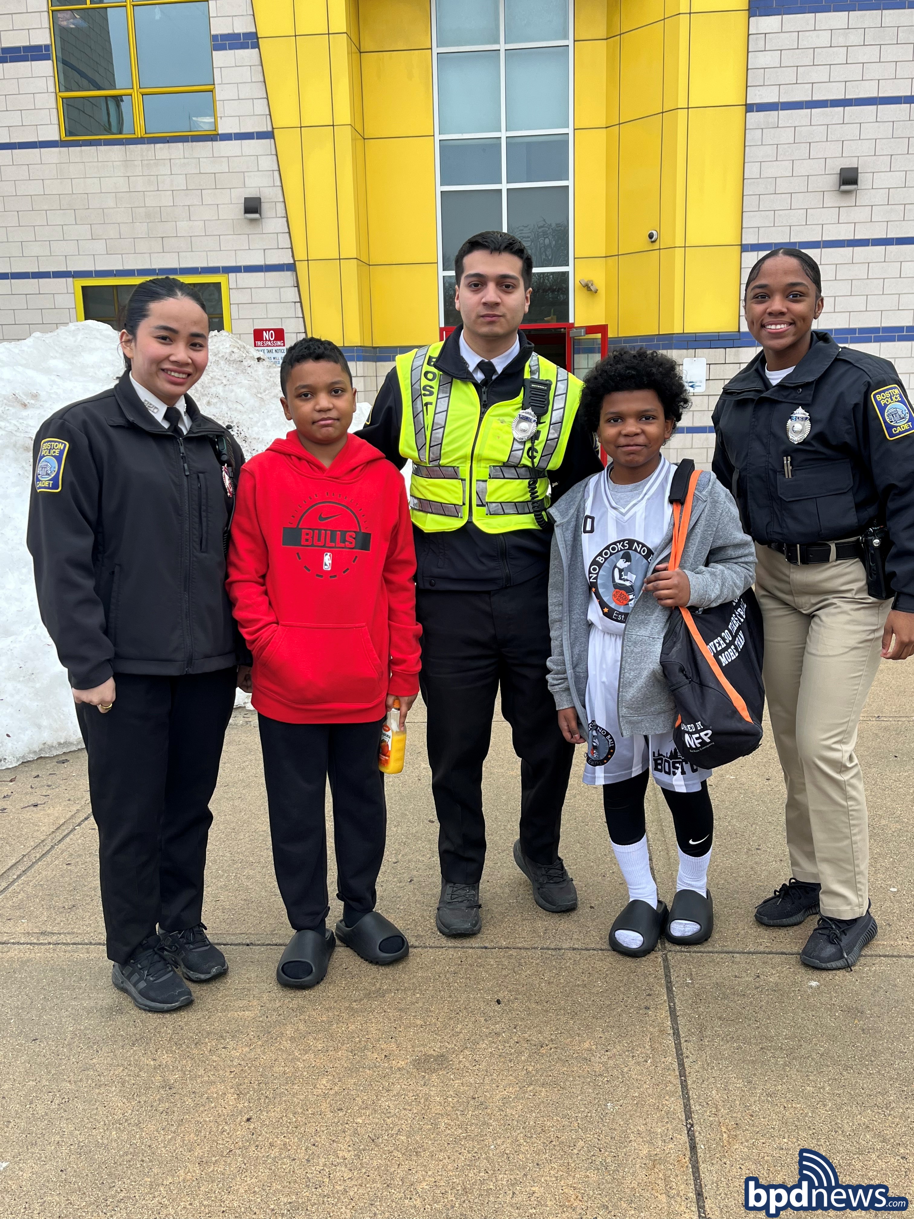 Three BPD Cadets pose for a picture with two young community members outside before they attend the No Books, No Ball Event.